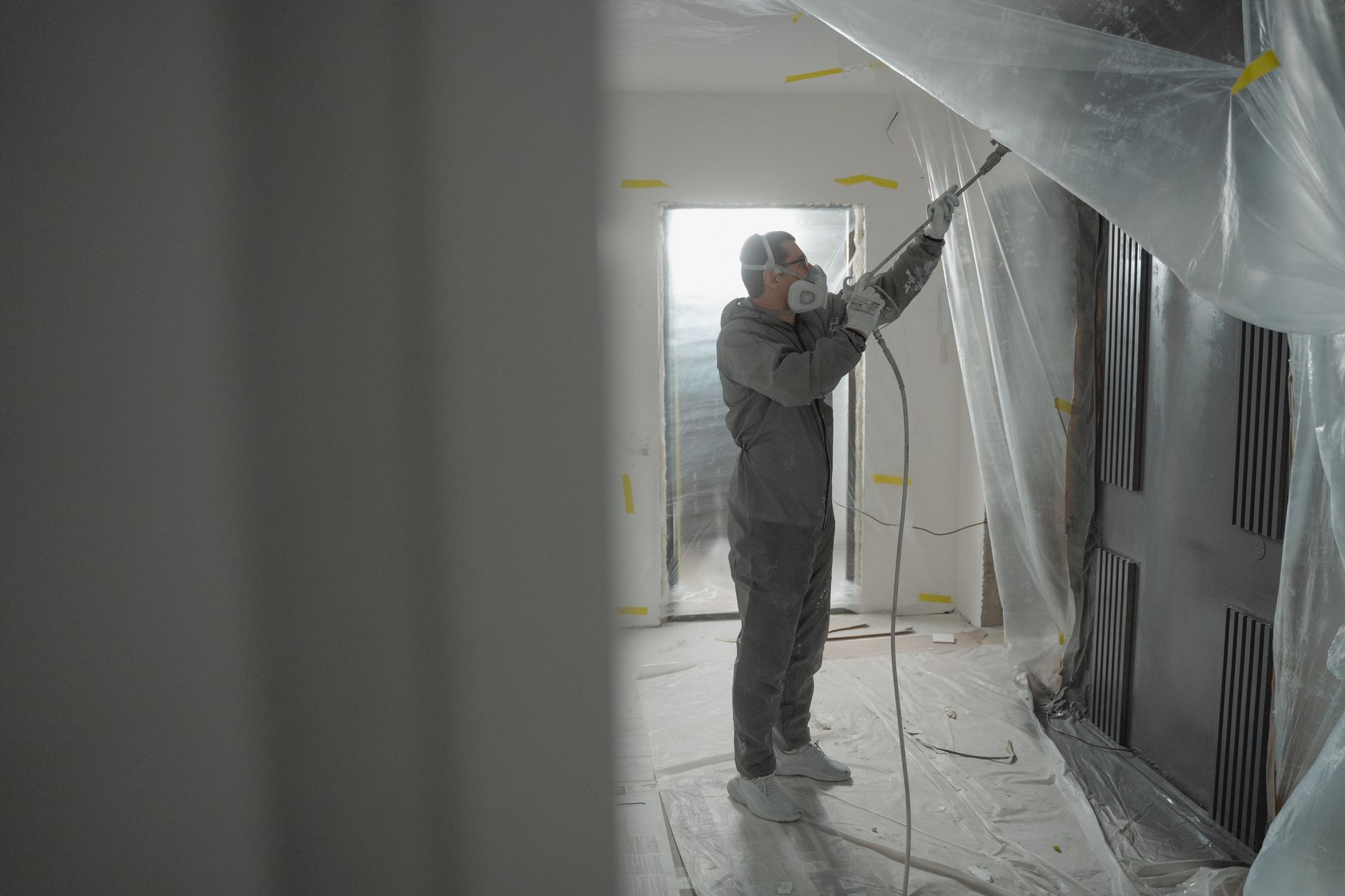 Man in protective gear spray painting a house's interior during renovation work in Long Beach, CA